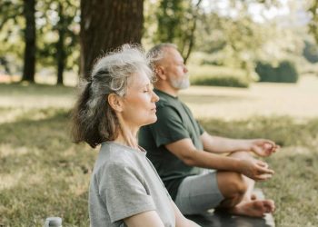 Stariji čovek i žena meditiraju u prirodi.