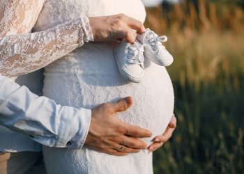 Trudna mlada drži patike za bebu dok je muž grli