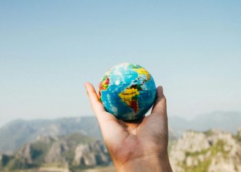 Osoba drži mali globus na dlanu i gleda na planinski pejzaž