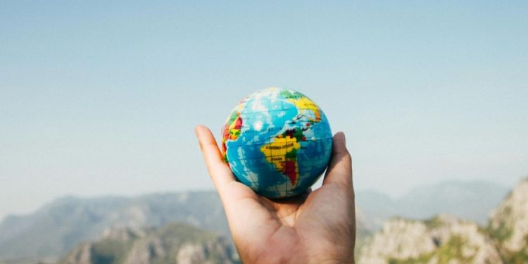 Osoba drži mali globus na dlanu i gleda na planinski pejzaž