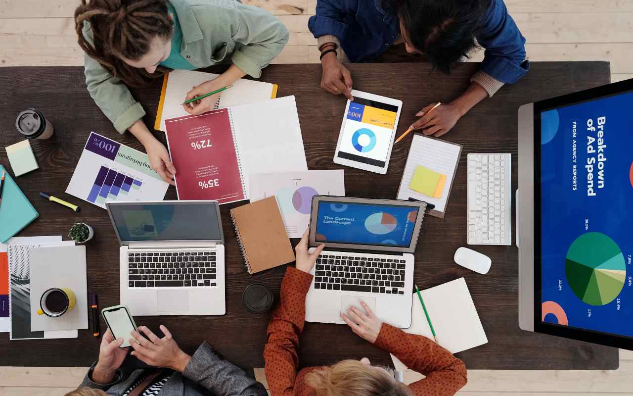 Kolege na poslu gledaju statističke podatke na laptopovima i tabletu