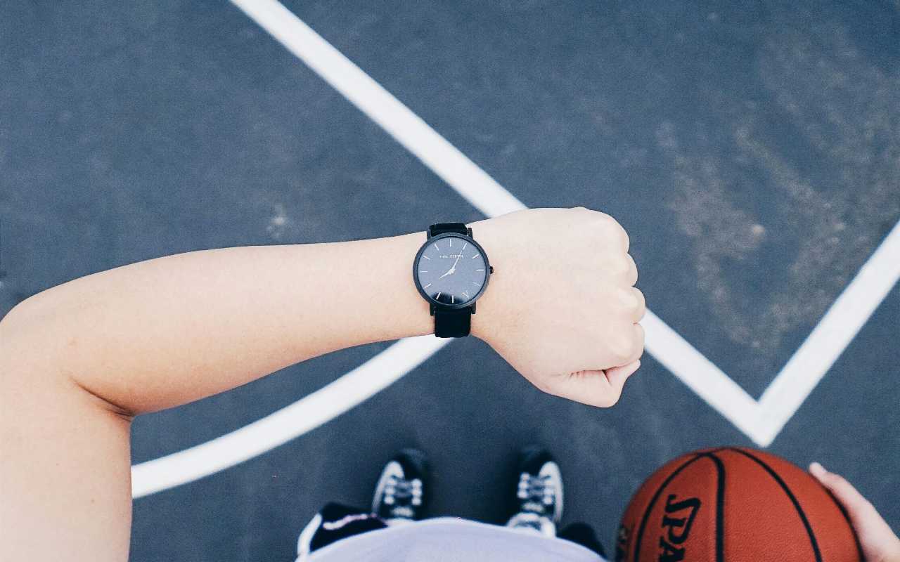 Čovek sa loptom u ruci gleda u sat.