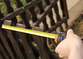 Ruka drži mernu traku i meri širinu drvene ograde.
