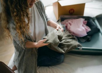 Osoba pakuje odeću u otvoreni kofer na krevetu