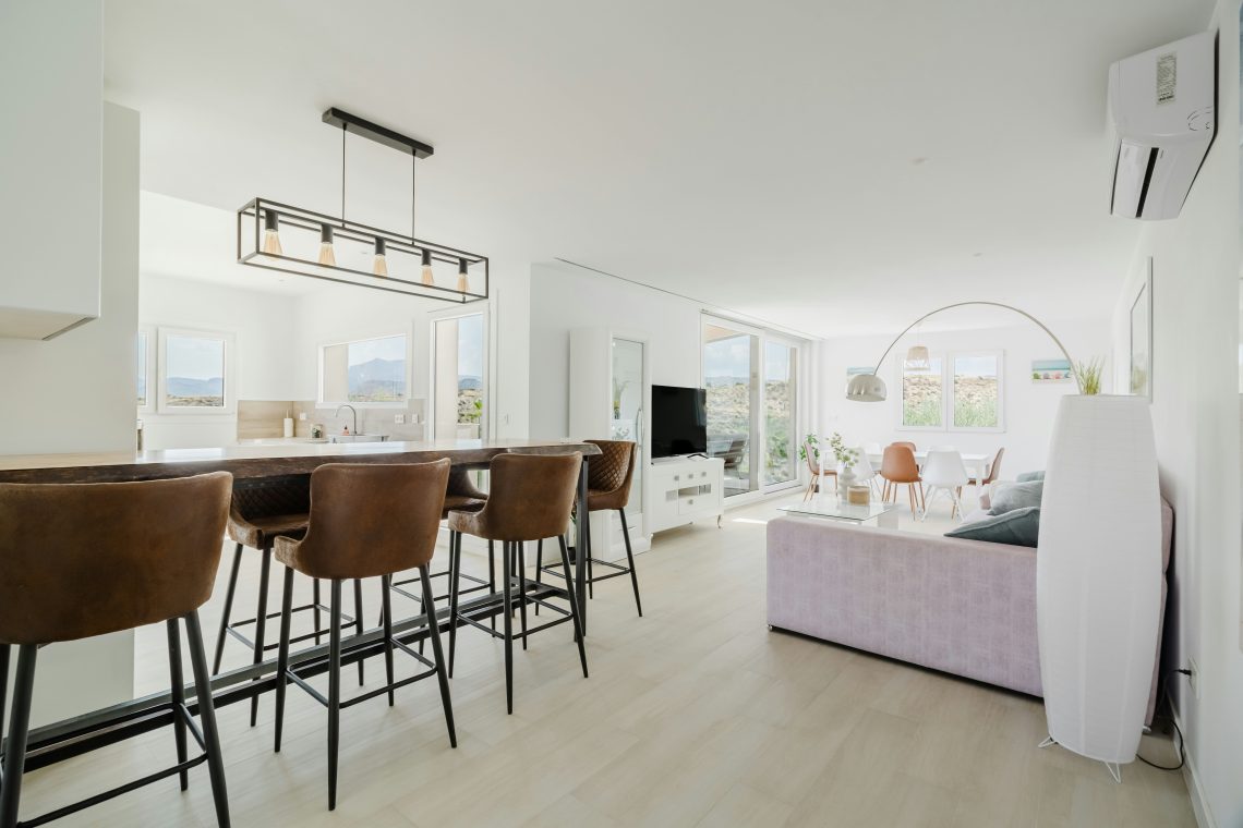 Smeđe barske stolice uz drveni kuhinjski šank u svetlom otvorenom dnevnom prostoru.