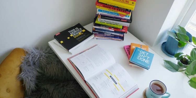 Radni sto sa otvorenom knjigom, naslagom knjiga i šoljom čaja