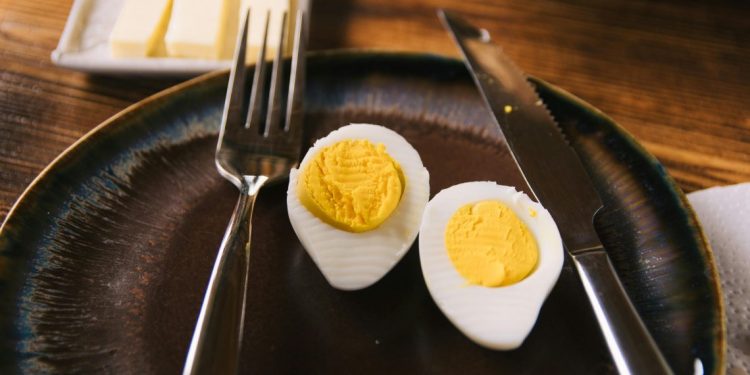 Prepolovljena tvrdo kuvana jaja na tamnom tanjiru sa viljuškom i nožem.