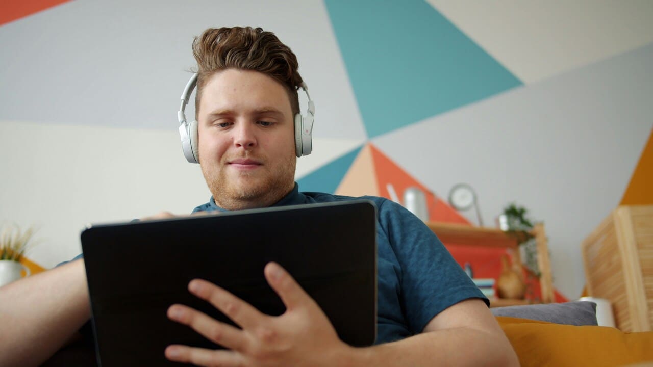 Muškarac sa slušalicama sedi na kauču i koristi tablet