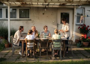 Porodični ručak na terasi dok žena sipa piće za sto