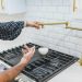 Ruka otvara slavinu od mesinga iznad šporeta dok voda kaplje u belu činiju