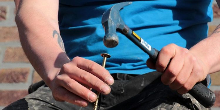 Ruke drže šraf dok čekić udara u njegovu glavu