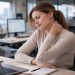 Žena sedi za kancelarijskim stolom i drži se za vrat