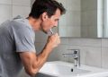 Muškarac se naginje nad lavabo i koristi četkicu za zube ispred ogledala