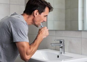 Muškarac se naginje nad lavabo i koristi četkicu za zube ispred ogledala