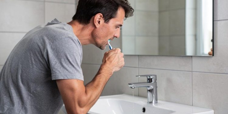 Muškarac se naginje nad lavabo i koristi četkicu za zube ispred ogledala