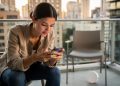 Žena na balkonu sedi i gleda u ekran mobilnog telefona
