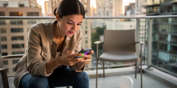 Žena na balkonu sedi i gleda u ekran mobilnog telefona