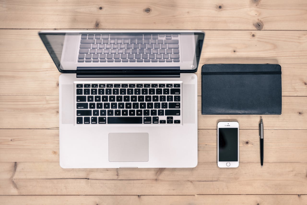 Macbook Pro pored srebrnog iPhone mobilnog telefona i notesa