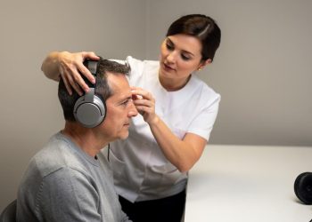 Žena podešava velike slušalice muškarcu koji sedi za stolom